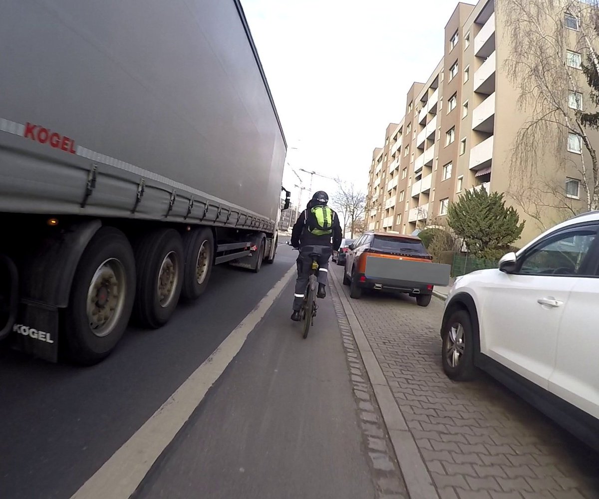 Ein Radfahrer auf einem schmalen, benutzungspflichtigen Radfahrstreifen im Dooring-Bereich wird von einem LKW mit 106 cm Abstand überholt. Gleichzeitig besteht die Gefahr, dass jederzeit unachtsam eine Fahrzeugtüre geöffnet wird.